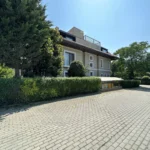 Opsa Klinik binasının ağaçlarla çevrili dış cephesi ve önündeki taş döşeli alan
